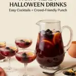 A glass pitcher filled with dark red punch, blackberries, and orange slices sits next to four coupe glasses containing the same drink.